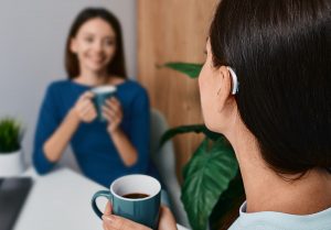Woman wearing a small hearing aid while talking and enjoying coffee with her friend 