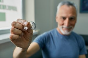 Smiling man holding an over-the-counter hearing aid