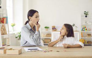 Mother helping her young daughter practice speech articulation exercises at home